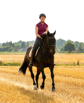 Eine Frau reitet auf einem Stoppelfeld im Galopp.